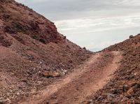 a dirt road near the mountain with hills in the background and sparse cloud filled sky