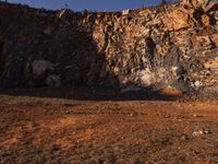 a horse stands at the base of a cliff and grazes near a fence that leads up to it