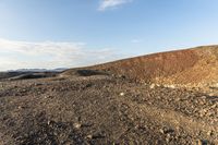 a dirt hill near a dry, grassy plain under a sky line with clouds and some sunlit