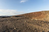 a dirt hill near a dry, grassy plain under a sky line with clouds and some sunlit