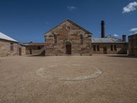 a large building with a circle in front of it on a gravel ground under a blue sky