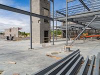 a large building under construction next to several empty benches on concrete floor space, blue sky and blue sky in background