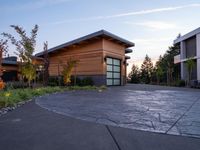 a building with a large garage and lots of greenery in the driveway area at dusk