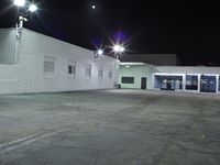 empty parking lot with the lighting on and building in the background with street lights on