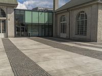 a sidewalk in front of some windows and a building with stone tiles and gravel paths in front of it