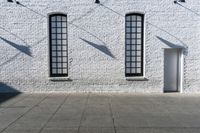 a building with three windows and a red fire hydrant outside it and shadows on the wall