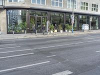 people standing outside a bus stop by the road with windows filled in pots, and bicycles parked nearby