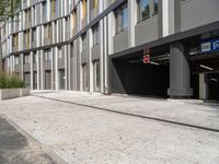 empty paved street near large tall modern building with glass windows on top of windows, near stone curb with plants, outside sidewalk in foreground