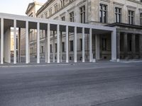 the large, empty sidewalk with multiple columns in front of the building with two signs