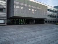 an empty area in front of a building with large windows and a stone floor underneath it