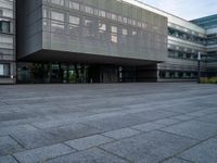 an empty area in front of a building with large windows and a stone floor underneath it