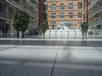 an empty walkway in front of a very tall building with glass walls and some trees