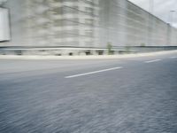 a long empty highway runs beside a gray building with many windows that blurry the view