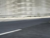 a long empty highway runs beside a gray building with many windows that blurry the view