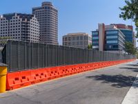 an orange fence separating off the road to traffic signals on it's sides and buildings in the background