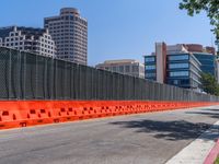 an orange fence separating off the road to traffic signals on it's sides and buildings in the background