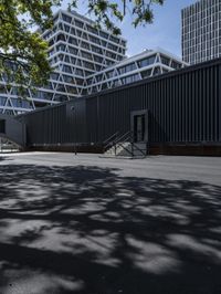 black building with stairs leading to two sides, in shade from some tree limbs and bushes