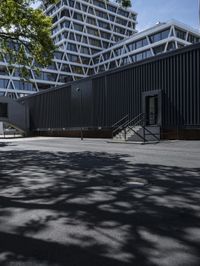 black building with stairs leading to two sides, in shade from some tree limbs and bushes