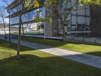 the park in front of an office building near a grass area with trees and benches