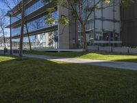 the park in front of an office building near a grass area with trees and benches