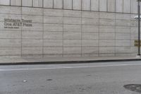 a man riding a skateboard down a sidewalk by a building with concrete siding and writing