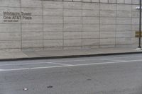 a man riding a skateboard down a sidewalk by a building with concrete siding and writing