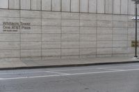 a man riding a skateboard down a sidewalk by a building with concrete siding and writing