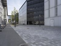 the sidewalk outside an empty industrial building is paved with gray tile pavers and a red bricked in area