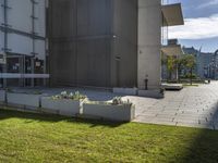 a concrete flowerbed in the grass between two buildings on the same building, with grass beside