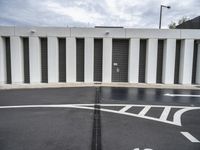 an empty parking lot with large white walls and black doors in the middle of the street