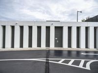 an empty parking lot with large white walls and black doors in the middle of the street