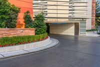 an empty parking lot in front of a tall building with red flowers growing in the middle