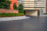 an empty parking lot in front of a tall building with red flowers growing in the middle