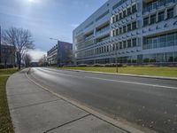 an empty highway leads towards a building with windows on it's sides and grass on the side