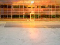 an empty parking lot with a large building behind it and a sun flare out from the window