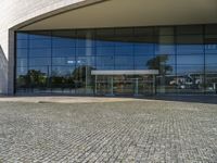 two people walking past a very large building with big glass doors and windows that look like a museum