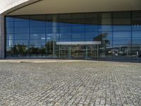 two people walking past a very large building with big glass doors and windows that look like a museum