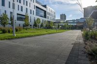 a city street surrounded by grass and tall buildings at the end of a street there is a paved pathway in front of the building