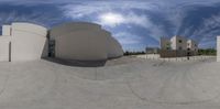 a photograph taken in fisheye position of buildings on a street corner, with sky and clouds above