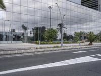 a building reflecting the clouds in a mirrored surface on the side of the street, with plants and trees