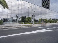 a building reflecting the clouds in a mirrored surface on the side of the street, with plants and trees