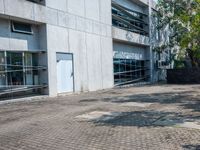 a sidewalk outside a building with no people walking or running through the building, some grass and trees