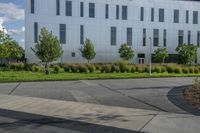 the man is riding his skateboard on the sidewalk near the building with trees, plants and bushes