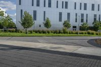 the man is riding his skateboard on the sidewalk near the building with trees, plants and bushes