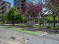 the green paint is painted on a bike path in front of an office building and large, trees