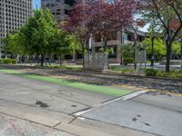 the green paint is painted on a bike path in front of an office building and large, trees