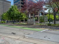 the green paint is painted on a bike path in front of an office building and large, trees