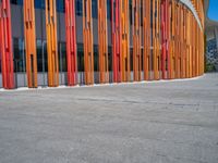 a concrete structure made into rows of orange and yellow poles are on a cement sidewalk