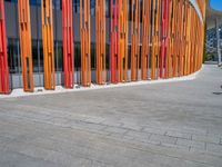 a concrete structure made into rows of orange and yellow poles are on a cement sidewalk