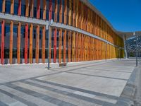 a concrete structure made into rows of orange and yellow poles are on a cement sidewalk